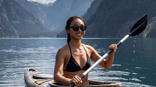 A woman wearing sunglasses while kayaking on a lake beside mountains