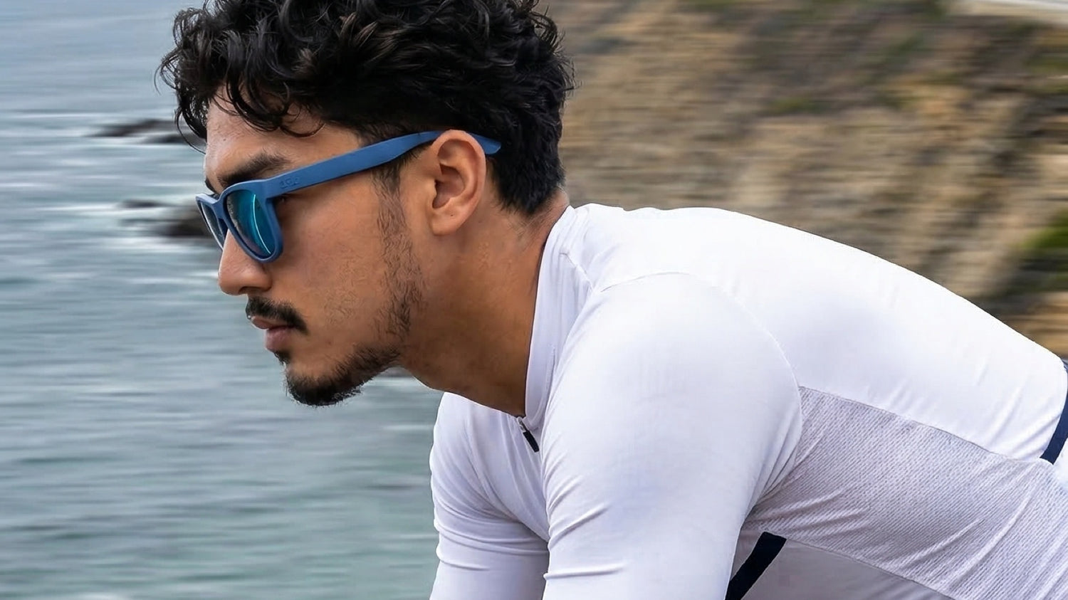 Cyclist wearing blue 2nu sunglasses near a coastal road, showing outdoor glare and road-use lens conditions.